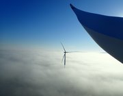 Windpark Erftstadt Windräder ragen aus einer dichten Nebeldecke in den blauen Himmel, im Vordergrund eine Rotorblattspitze.